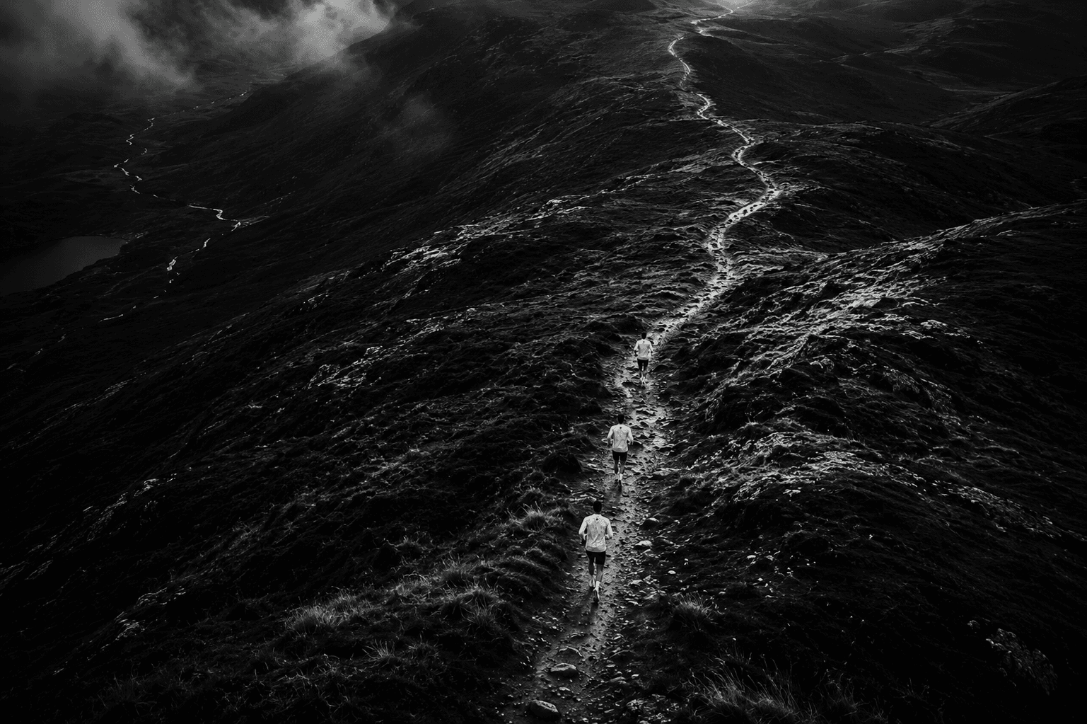 Aerial view of runners ascending a remote mountain ridge under heavy cloud