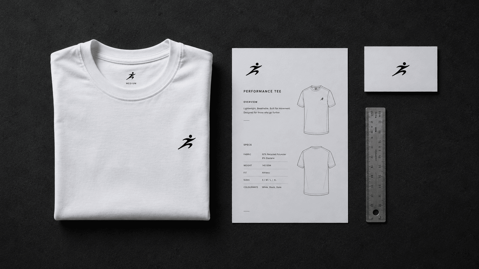 The MALIN press kit: a folded performance tee, printed spec sheet, logo card and steel ruler on a charcoal surface